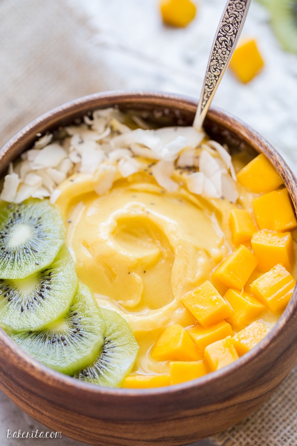 Pineapple Mango Smoothie in a wooden bowl topped with kiwi slices, mango chunks, coconut flakes and chia seeds.