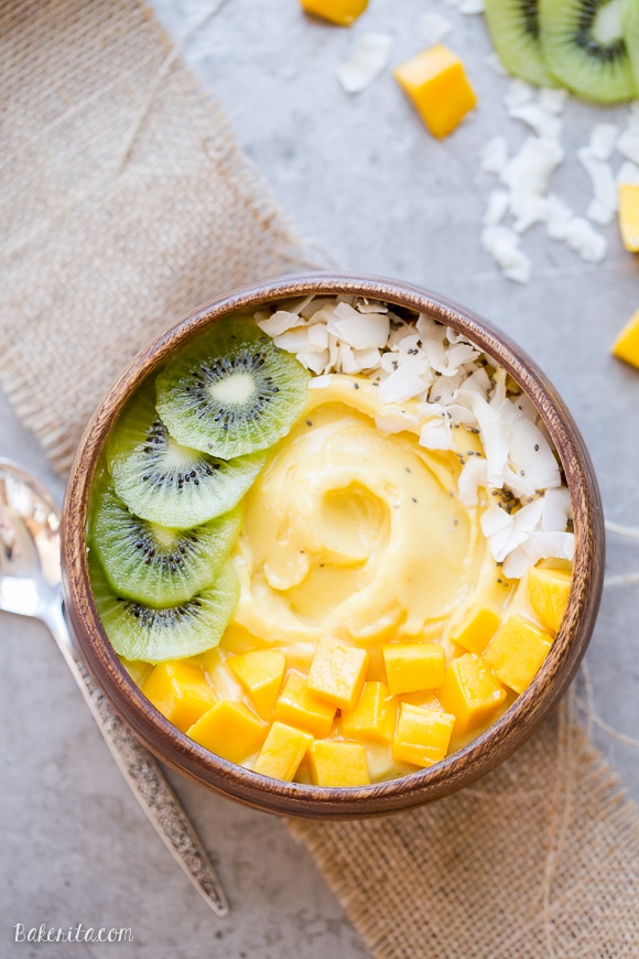 Pineapple Mango Smoothie in a wooden bowl topped with kiwi slices, mango chunks, coconut flakes and chia seeds.