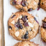 Large, round blueberry cookies topped with whole blueberries and almond slices are arranged closely on a parchment-lined baking sheet. These golden brown treats have a rustic appearance, making them perfect breakfast cookies for your morning routine.