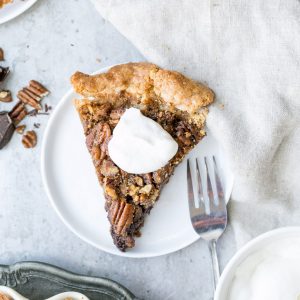 This Paleo Chocolate Pecan Pie has a flaky grain-free pie crust and a layer of chocolate ganache! This gluten-free and refined sugar-free pie is gooey, crunchy, and the perfect addition to your holiday dessert line-up.