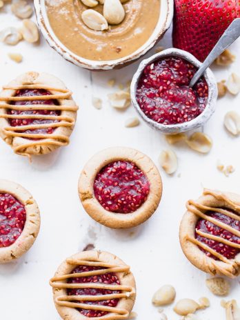 These Peanut Butter & Jelly Tartlets are made with just SEVEN ingredients! They have a crunchy peanut butter cookie crust, filled with an easy strawberry chia jam and topped with even more peanut butter. These gluten-free, grain-free, and vegan tartlets are as cute as they are delicious!