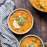 Two bowls of Vegan Red Lentil Soup topped with microgreens and lemon, with a striped napkin. Also a pot of healthy lentil soup next to the bowls!