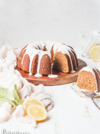 Gluten-Free Vegan Lemon Cake on wooden plate, with one slice taken out. Slice is in the front on a plate, with vegan lemon glaze and lemon garnish.