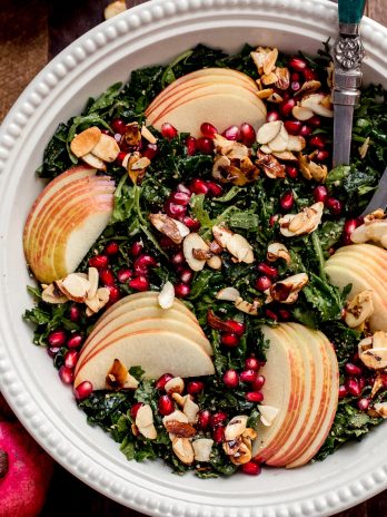 This Autumn Kale Harvest Salad brings together the best of fall's produce into a beautiful salad. With thinly sliced kale, pomegranate seeds, Honeycrisp apple slices, candied almond slices, and tossed in a lusciously sweet and tangy Apple Cider Vinaigrette. It's healthy, simple, beautiful, and the perfect accompaniment to your holiday meal or autumn dinner table.