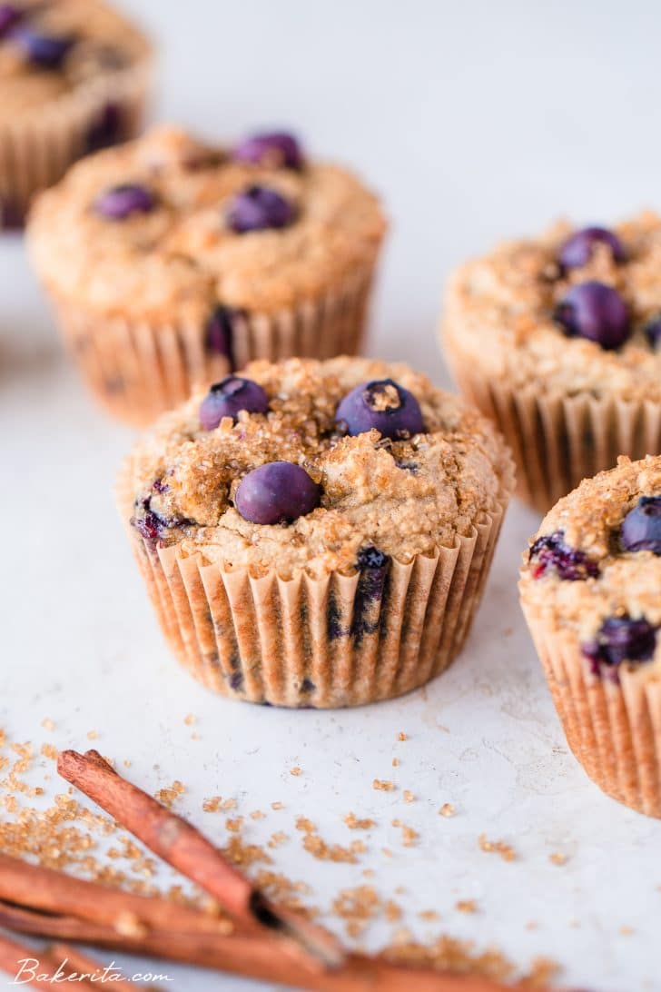 Five gluten-free vegan blueberry muffins on a white background, all in parchment liners.