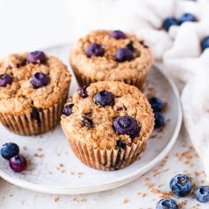 Three blueberry muffins on a plate with a white background.