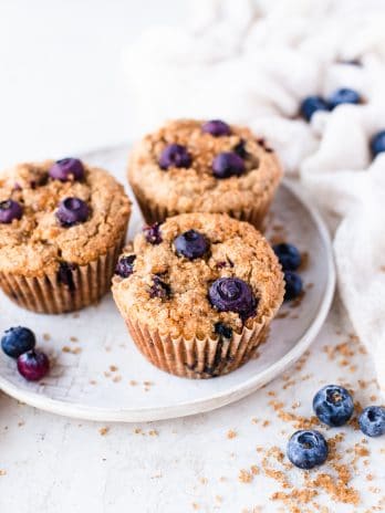 Three blueberry muffins on a plate with a white background.