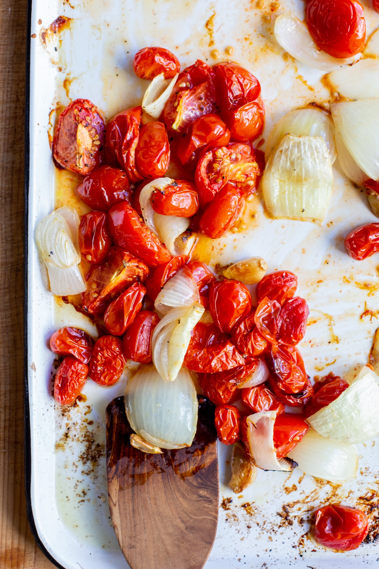 Roasted tomatoes, onions, and garlic on a white sheet pan.