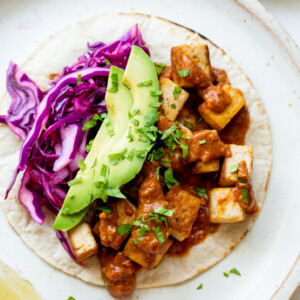 One sriracha tofu taco on a ceramic plate, topped with avocado, red cabbage, salsa, and cilantro.