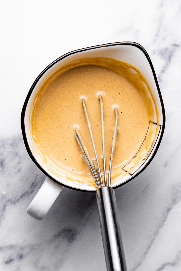 Creamy miso sesame dressing in a measuring cup with a whisk in it.