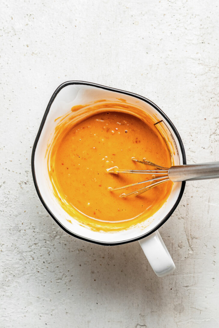 Peanut sauce salad dressing in a large measuring cup from above with a whisk in it.